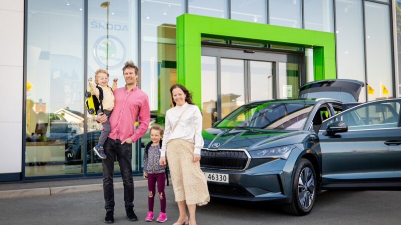 Használt elektromos autó átvétele: család a frissen átvett Škoda Enyaq iV mellett a márkakereskedés előtt